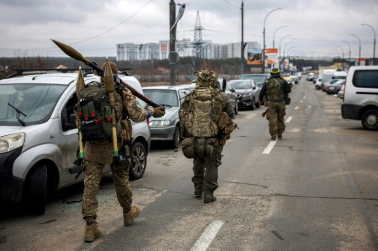 2022 年 3 月 13 日、キエフの北西にあるイルピンの街に向かって歩くウクライナの軍人は、ロケット推進手榴弾と狙撃銃を持っています。