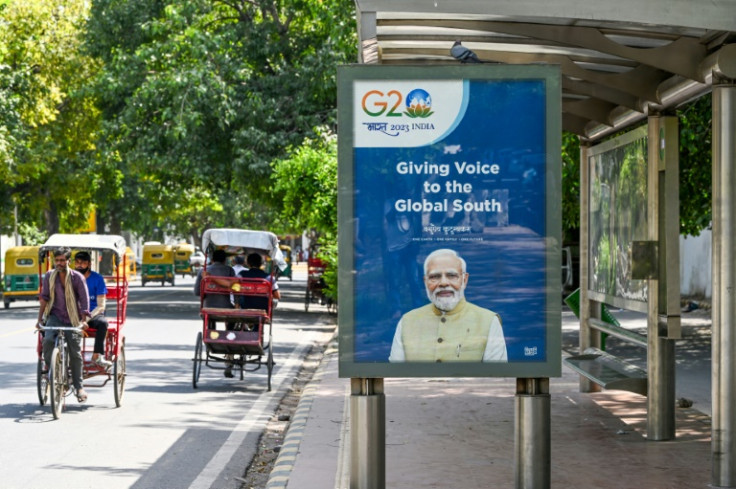 ニューデリーで、インドのナレンドラ・モディ首相の肖像画が描かれたG20ポスターが貼られたバス停付近をサイクル人力車で移動する人々。