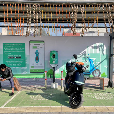 2022年2月12日、インドのニューデリーにある電気自動車充電ステーションで、電動スクーター「オラ」を充電しながら携帯電話をチェックする男性。