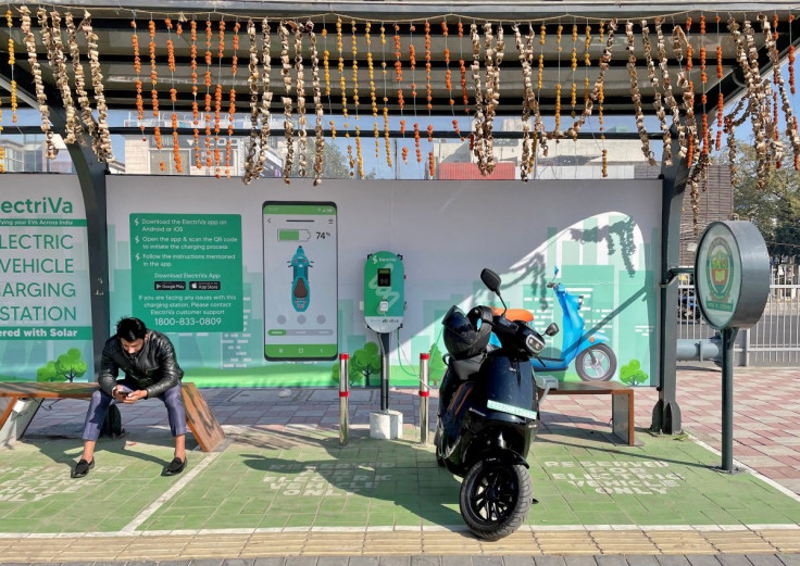 2022年2月12日、インドのニューデリーにある電気自動車充電ステーションで、電動スクーター「オラ」を充電しながら携帯電話をチェックする男性。